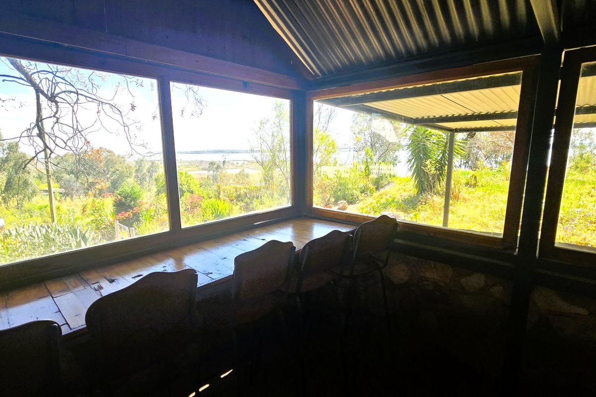A rustic living space featuring expansive windows with scenic garden views, a built-in timber bench, and a distinctive corrugated metal ceiling.