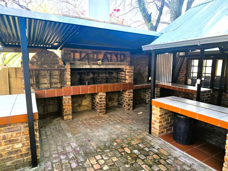 Outdoor entertainment area featuring a large built-in brick braai, tiled prep counters, and a covered patio structure with brick paving.