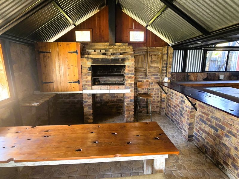 Rustic covered outdoor entertainment area featuring a built-in brick braai, bar counter, and exposed timber roof structure.