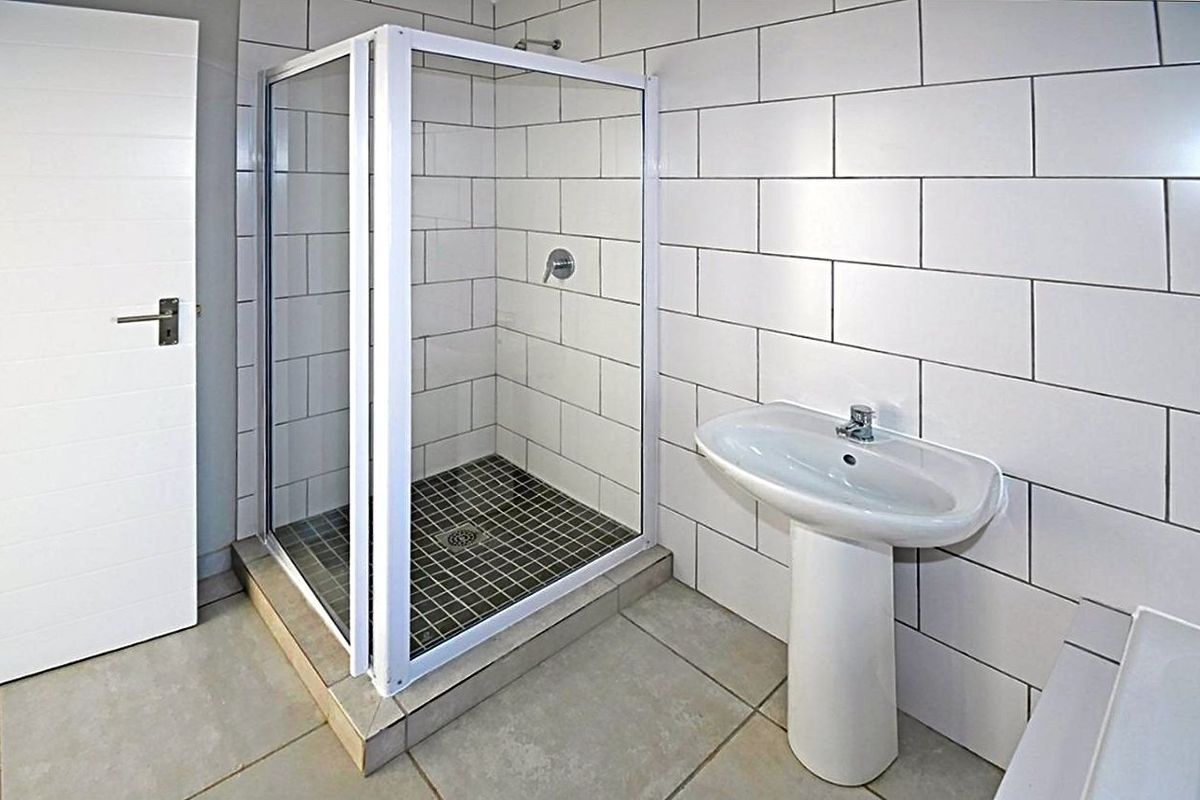 A clean, modern bathroom featuring a glass-enclosed shower, white subway-style wall tiles, and a classic pedestal basin.