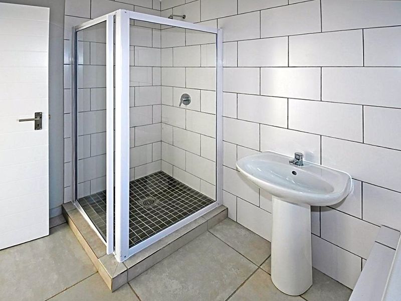 A clean, modern bathroom featuring a glass-enclosed shower, white subway-style wall tiles, and a classic pedestal basin.