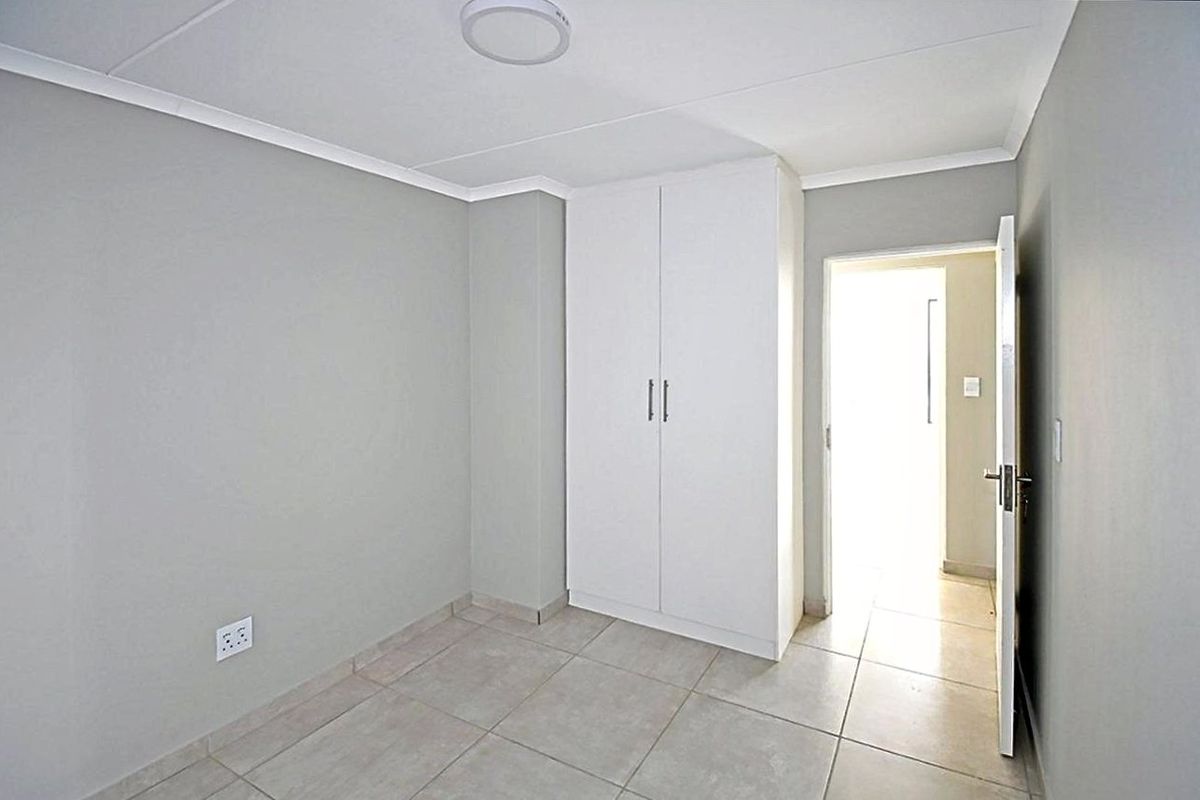 A clean, empty bedroom featuring neutral grey walls, tiled flooring, and a built-in white wardrobe, offering a blank canvas for personalization.