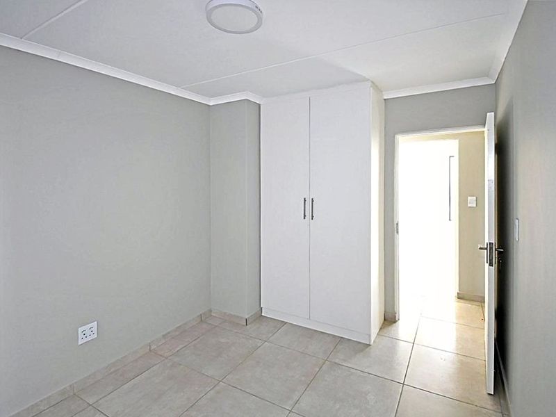 A clean, empty bedroom featuring neutral grey walls, tiled flooring, and a built-in white wardrobe, offering a blank canvas for personalization.