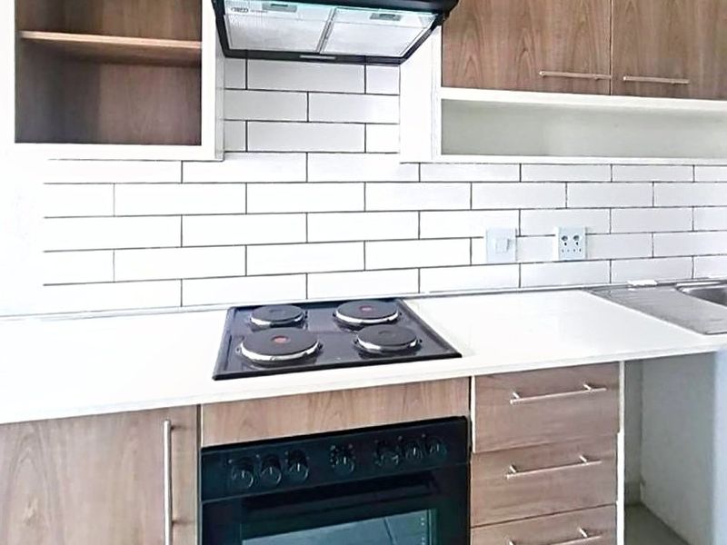 Modern kitchen featuring wood-finish cabinetry, a subway tile backsplash, built-in electric hob, oven, and extractor fan with clean white countertops.