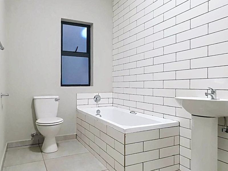 A clean, modern bathroom featuring a pedestal basin, a standard toilet, and a bathtub with white subway tile surround.