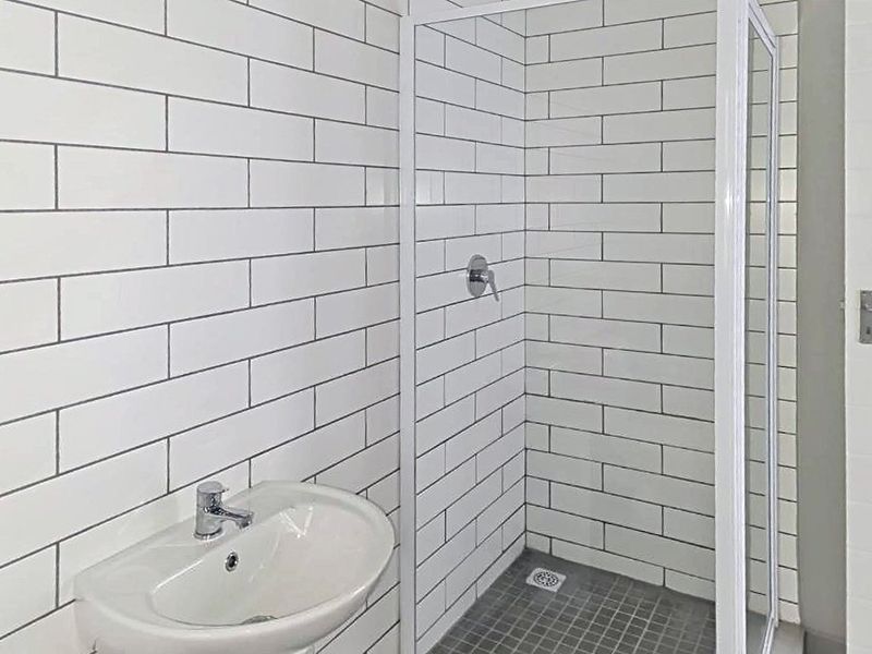 A clean, modern bathroom featuring white subway wall tiles, a glass shower enclosure, and a pedestal basin with contemporary fixtures.