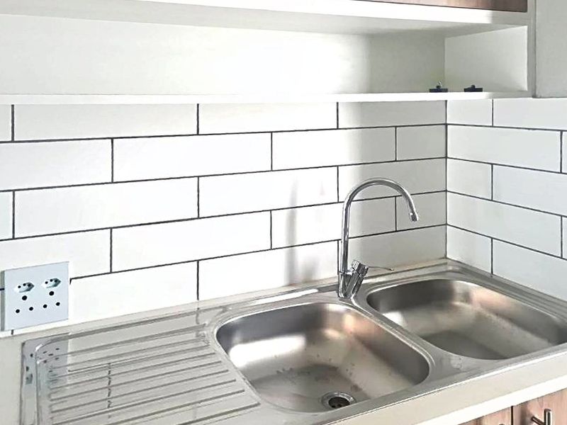 A clean kitchen area featuring a stainless steel double sink with a modern gooseneck faucet and a classic white subway tile backsplash.