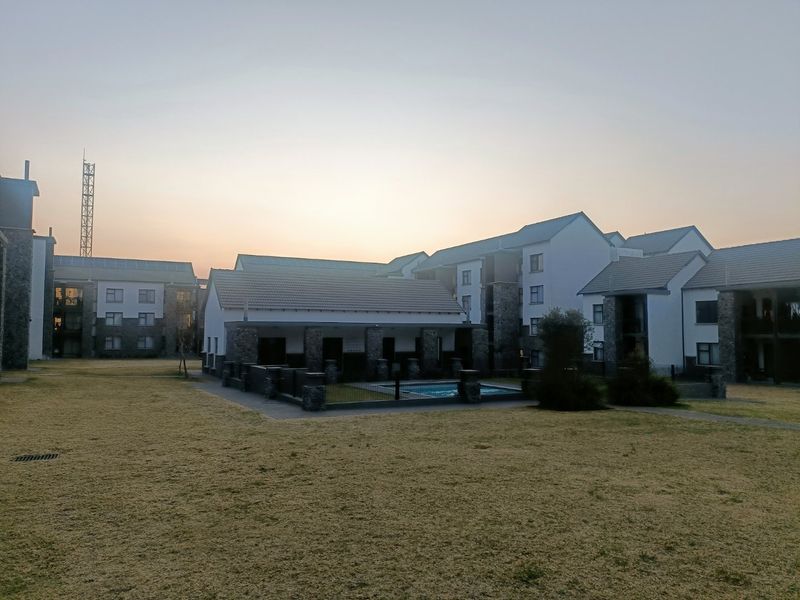 Exterior view of the apartment complex featuring a communal swimming pool, landscaped garden areas, and modern stone and plaster building facades.