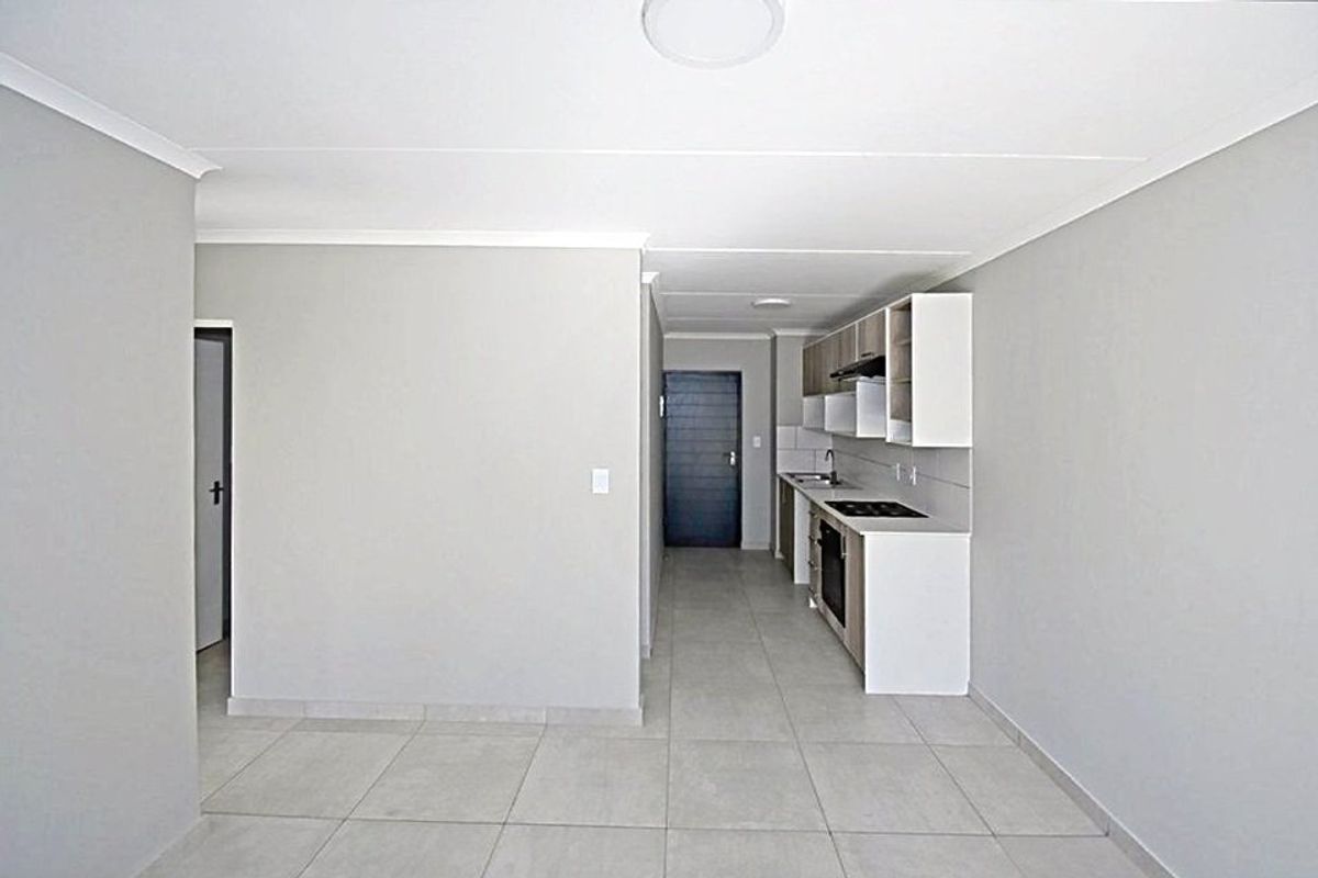 An open-plan living area featuring a modern kitchen with built-in cabinetry, electric hob, oven, and tiled flooring throughout.