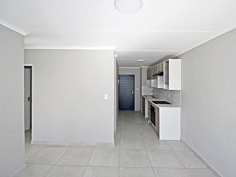 An open-plan living area featuring a modern kitchen with built-in cabinetry, electric hob, oven, and tiled flooring throughout.