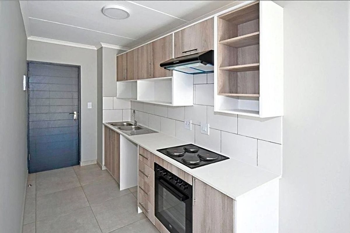 Modern kitchen featuring light wood-tone cabinetry, white countertops, built-in electric oven and hob, extractor fan, and neutral tiled flooring.