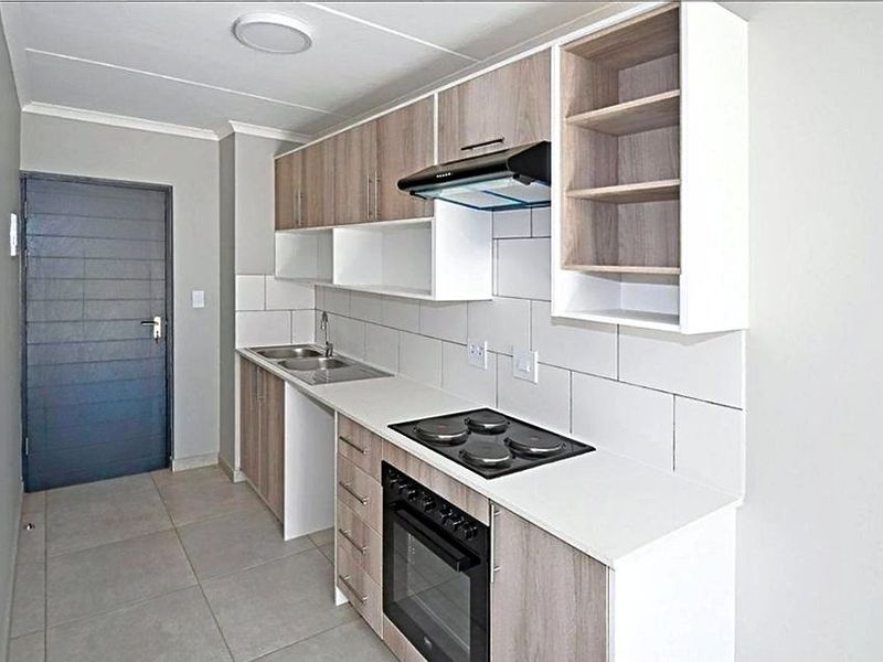 Modern kitchen featuring light wood-tone cabinetry, white countertops, built-in electric oven and hob, extractor fan, and neutral tiled flooring.