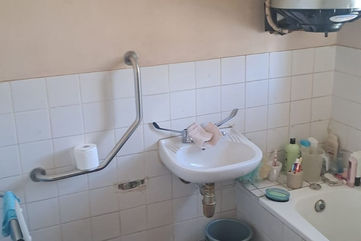 A dated bathroom featuring a wall-mounted basin, bathtub, toilet, and grab rail, requiring significant renovation and modernization of fixtures and finishes.