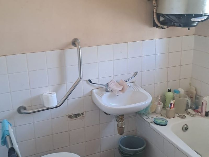 A dated bathroom featuring a wall-mounted basin, bathtub, toilet, and grab rail, requiring significant renovation and modernization of fixtures and finishes.