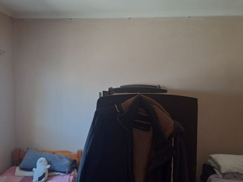 A bedroom featuring a window and ceiling cornice, currently showing signs of wear and requiring cosmetic updates.