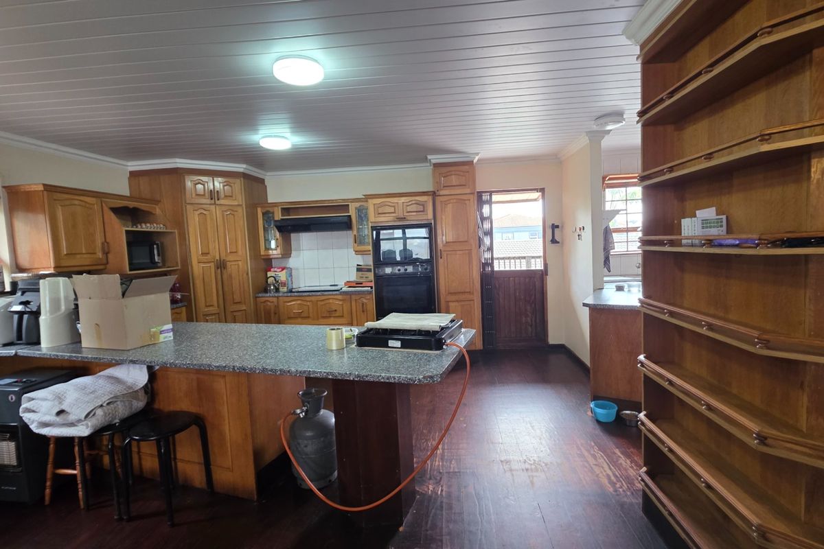 Spacious kitchen featuring extensive wooden cabinetry, built-in oven, extractor fan, and a central island with laminate countertops, finished with timber flooring and ceiling.