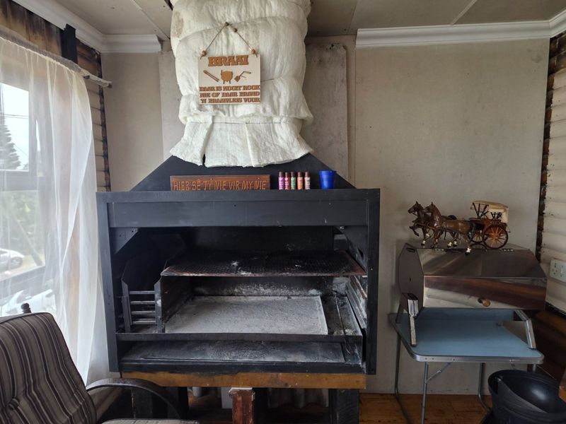 An indoor entertainment area featuring a built-in braai with chimney flue and timber wall cladding, requiring some maintenance and cosmetic updates.
