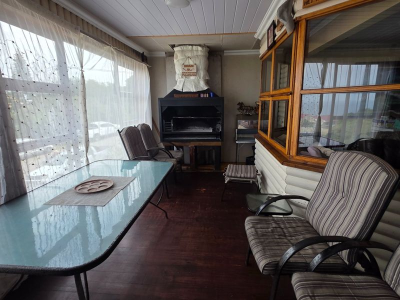 Enclosed patio area featuring a built-in braai, timber wall cladding, and large windows providing ample natural light.