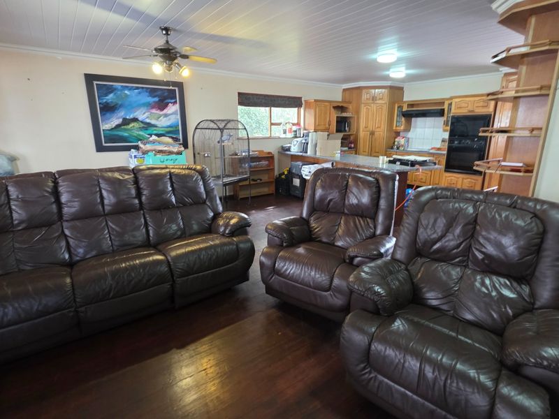 Open-plan living area featuring wooden flooring, a ceiling fan, and a functional kitchen with built-in cabinetry, oven, and island workspace.