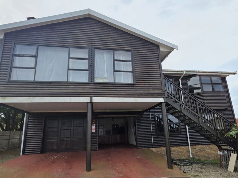 A two-story log-style house featuring an elevated living area, external staircase, and ground-level garage space with a concrete driveway.