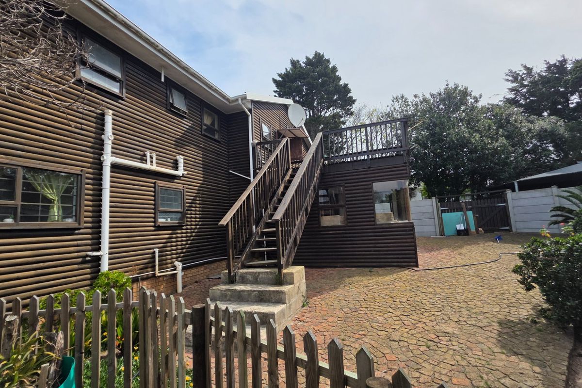 Rear view of a log-style house featuring a paved courtyard, a raised wooden deck, and an external staircase leading to the upper level.