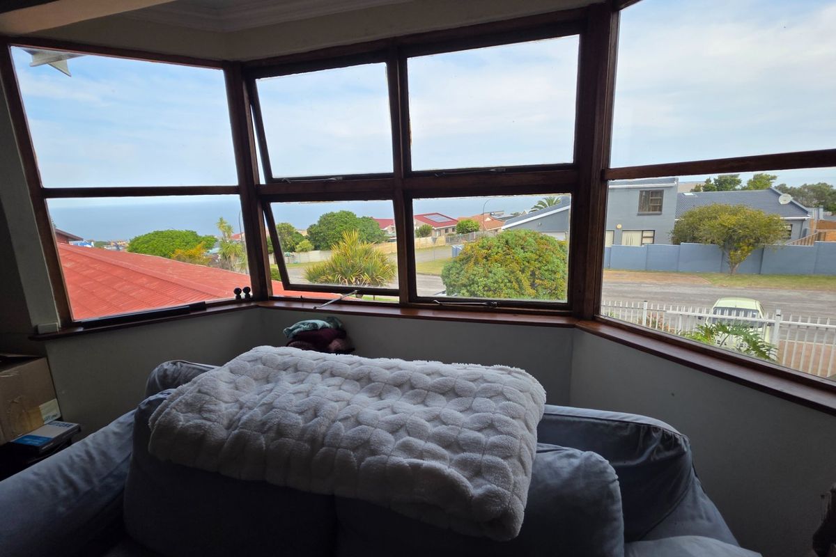 A living area featuring a large timber-framed bay window that provides expansive views of the surrounding neighborhood and distant coastline.