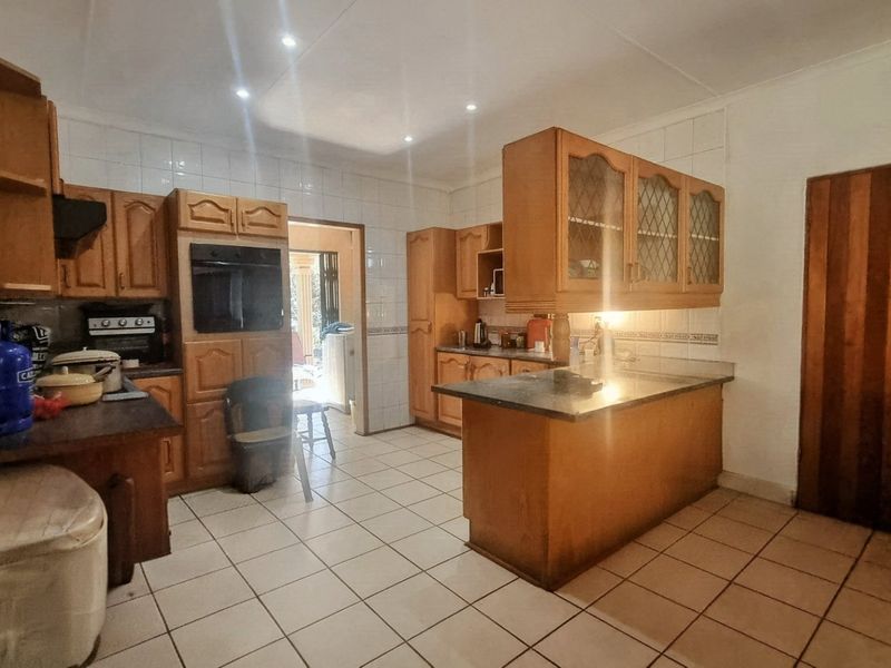 A functional kitchen featuring wooden cabinetry, built-in oven, extractor fan, and a central island with tiled flooring and backsplash.