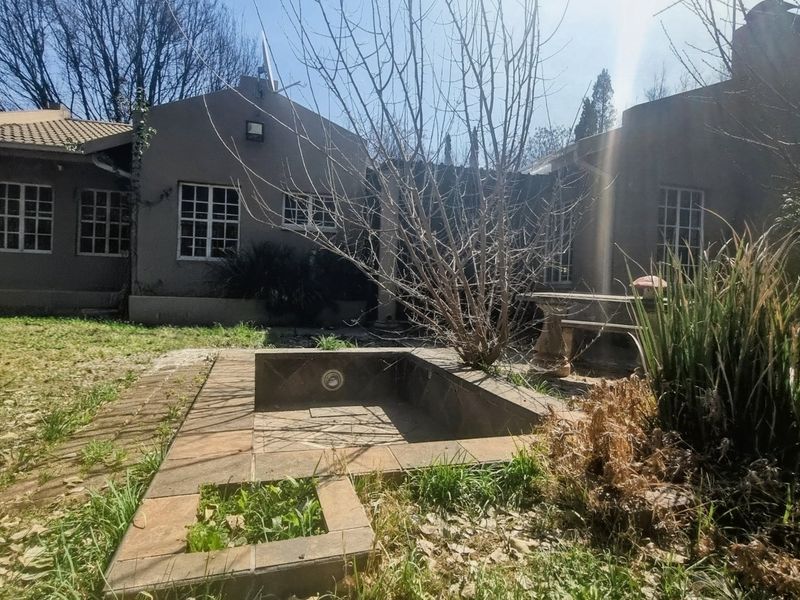 Rear view of the house featuring a paved patio area, a built-in water feature, and a garden requiring maintenance.