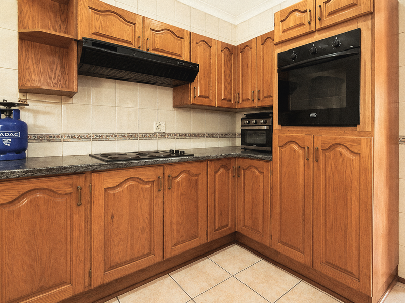 A functional kitchen featuring traditional wooden cabinetry, built-in oven, electric hob, extractor fan, and tiled finishes throughout.