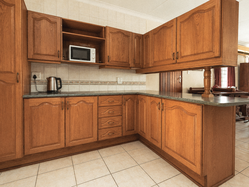 A functional kitchen featuring traditional wood-finish cabinetry, laminate countertops, and tiled flooring, offering a classic layout with ample storage space.