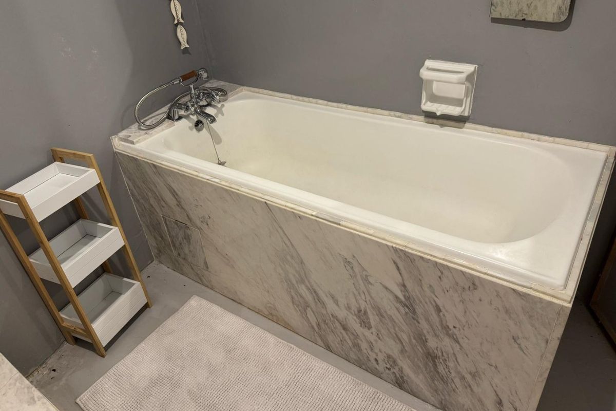 A bathroom featuring a bathtub with a marble-look tiled surround, chrome mixer tap, and built-in soap dish.