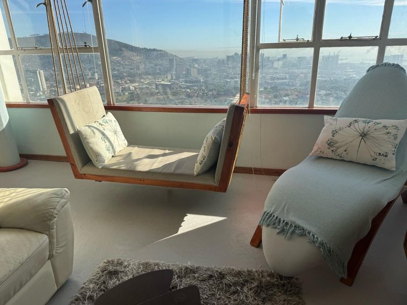 A bright living area featuring expansive steel-framed windows offering panoramic city views and durable concrete flooring.