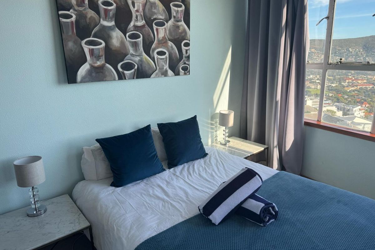 A bright bedroom featuring a large window with expansive city and mountain views, neutral wall finishes, and ample natural light.