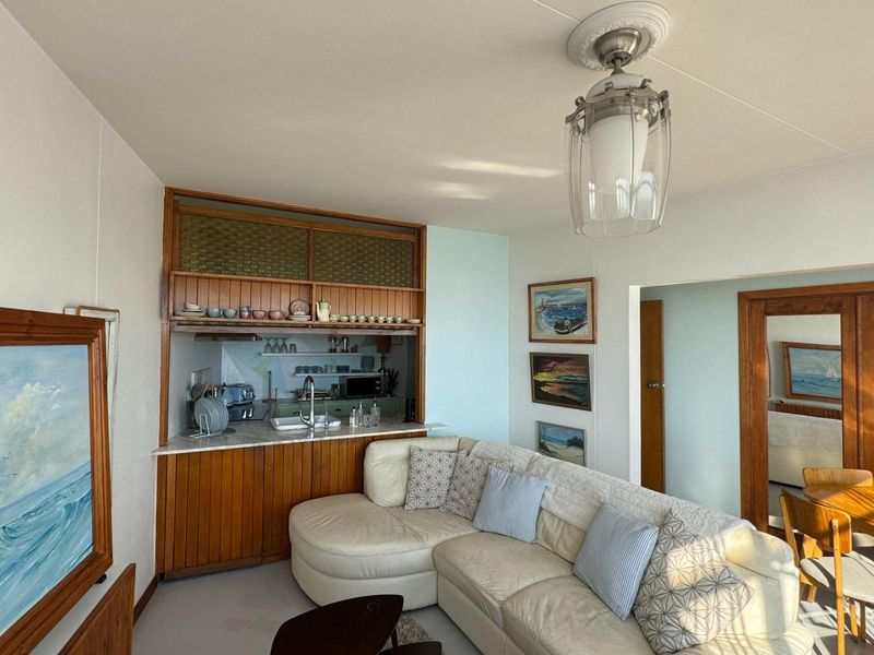 Open plan living area featuring a compact kitchen with built-in wooden cabinetry and a functional sink, connected to the main living space.