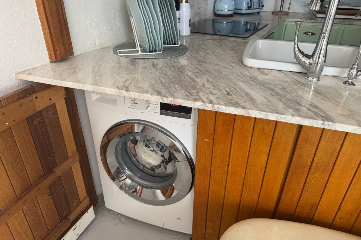 Compact kitchen area featuring a marble-look countertop, integrated washing machine, induction hob, and a classic undermount sink with a chrome faucet.