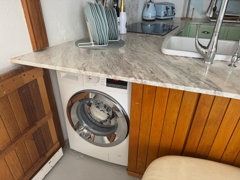 Compact kitchen area featuring a marble-look countertop, integrated washing machine, induction hob, and a classic undermount sink with a chrome faucet.