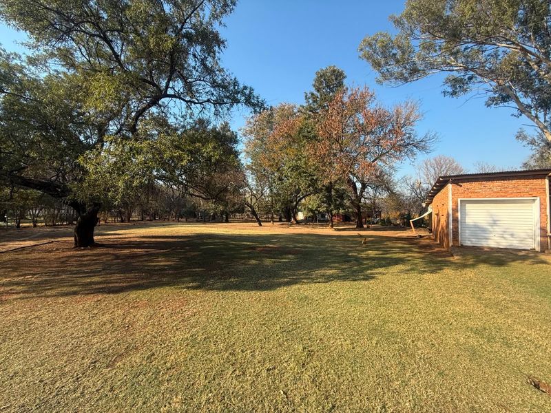 A spacious, well-maintained garden area featuring mature trees, expansive lawn, and a detached brick garage with a sectional door.