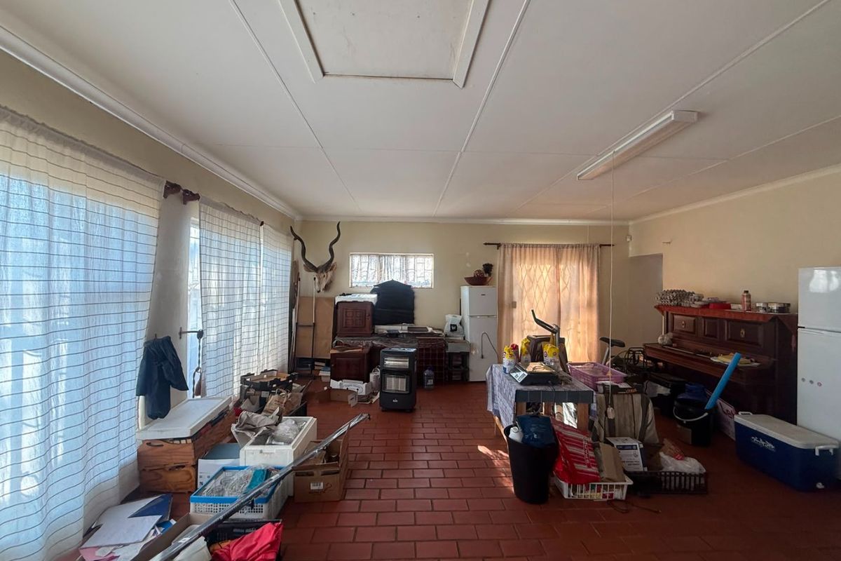 A spacious living area featuring traditional terracotta-style floor tiles and a functional ceiling access hatch, offering a blank canvas for renovation.