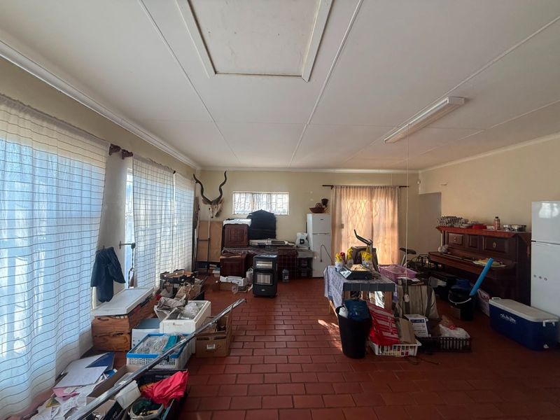 A spacious living area featuring traditional terracotta-style floor tiles and a functional ceiling access hatch, offering a blank canvas for renovation.