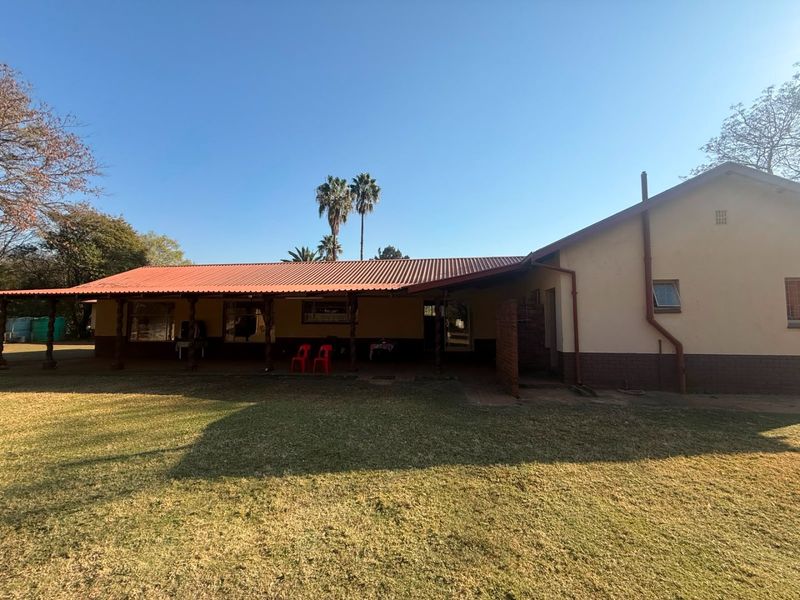 Rear view of the house featuring a large covered patio area, corrugated metal roofing, and a spacious lawn.