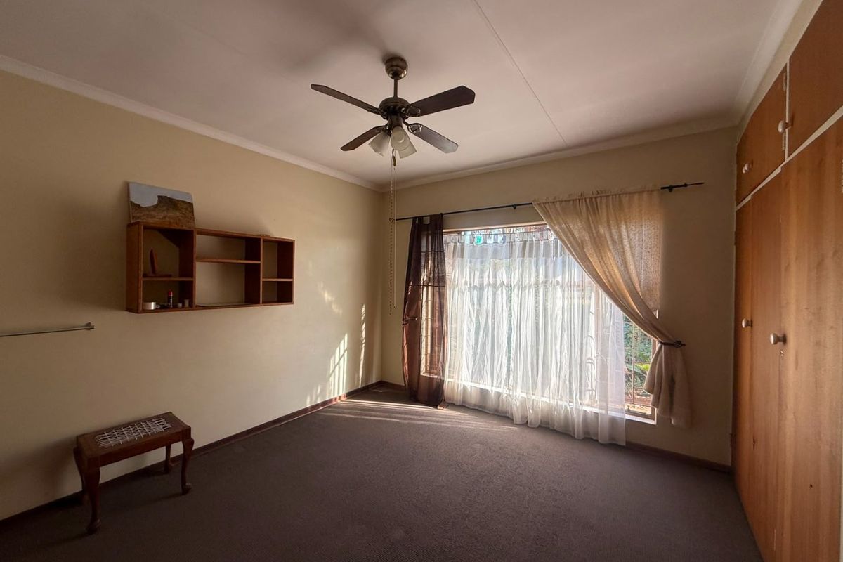 A spacious bedroom featuring built-in wooden cupboards, a ceiling fan, and large windows allowing for natural light.