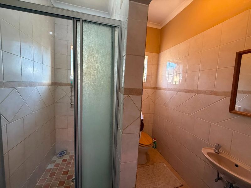 A functional bathroom featuring a shower enclosure, toilet, and wall-mounted basin with neutral ceramic tiling throughout.