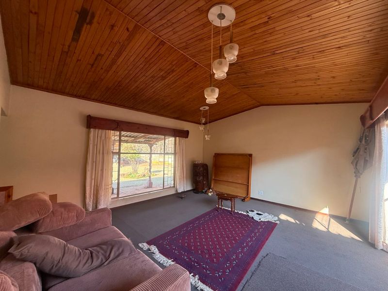 Spacious living room featuring a vaulted timber-clad ceiling, large picture window providing natural light, and carpeted flooring.