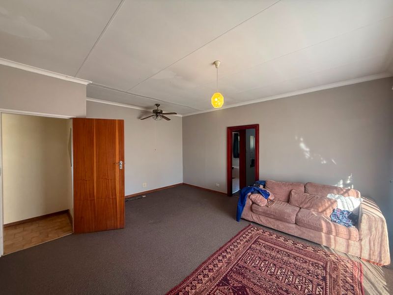 A living room featuring carpet flooring, a ceiling fan, and a pendant light, with visible signs of wear and ceiling water staining.
