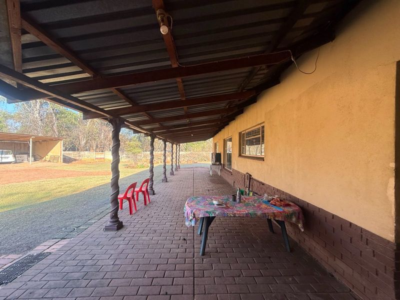 A spacious covered patio featuring brick paving, decorative spiral columns, and a corrugated metal roof, overlooking the rear garden area.