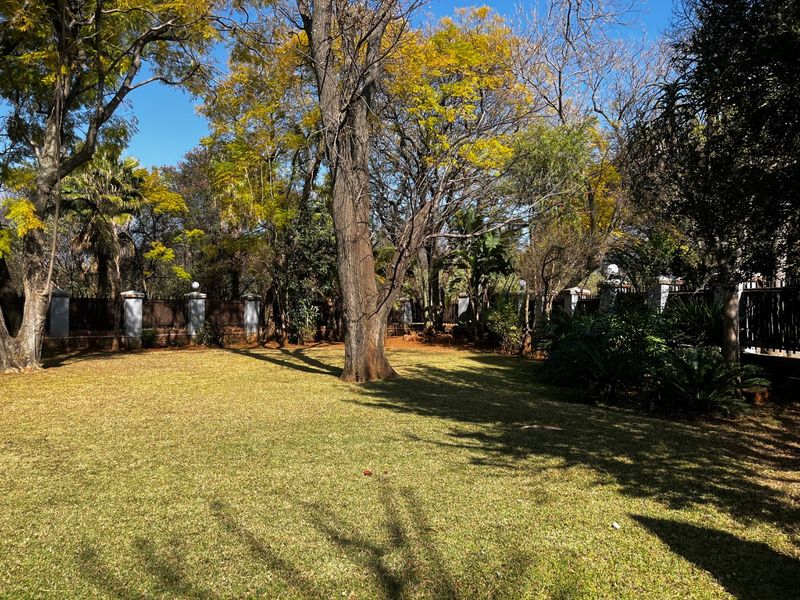 A spacious, well-maintained garden featuring a large lawn area, mature trees, and a secure perimeter wall.