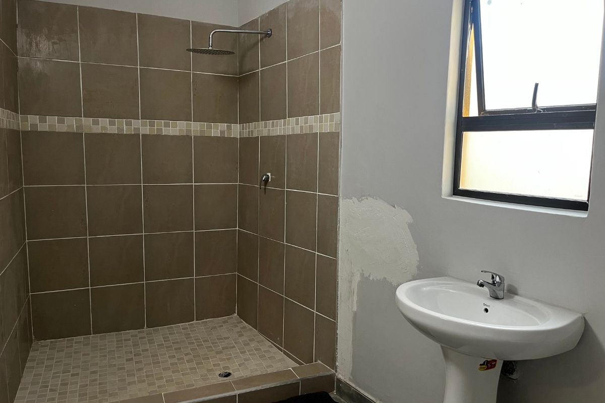 A functional bathroom featuring a walk-in shower with tiled surround and a pedestal basin, currently requiring minor wall finishing work.