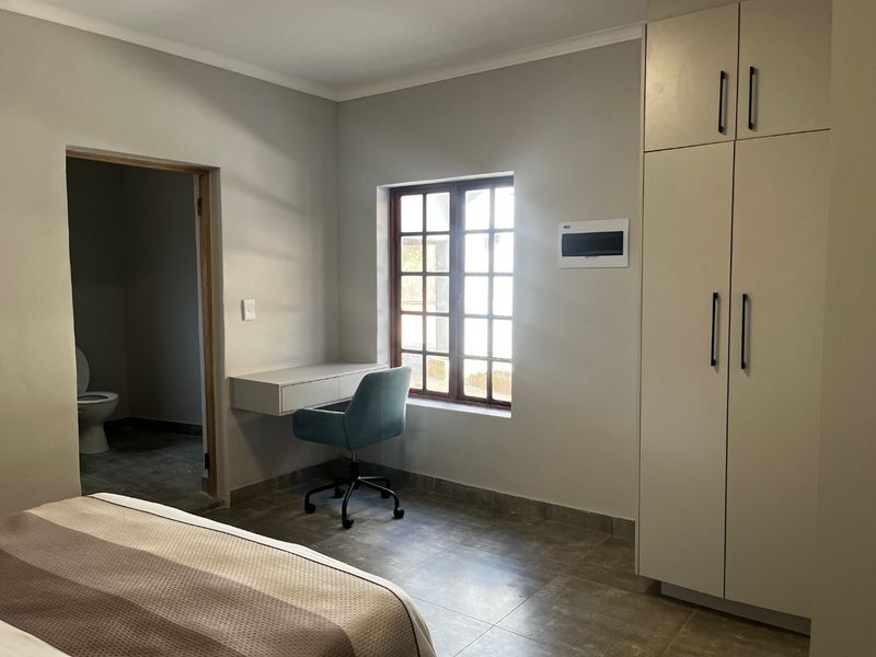 A well-maintained bedroom featuring tiled flooring, a built-in wardrobe, a wall-mounted desk, and direct access to an en-suite bathroom.