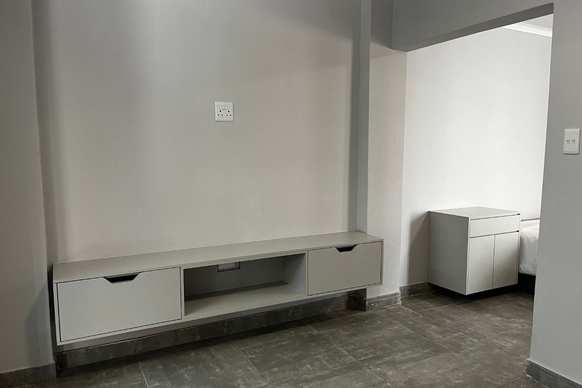 A clean, modern bedroom space featuring neutral grey walls, tiled flooring, and minimalist built-in cabinetry for storage.