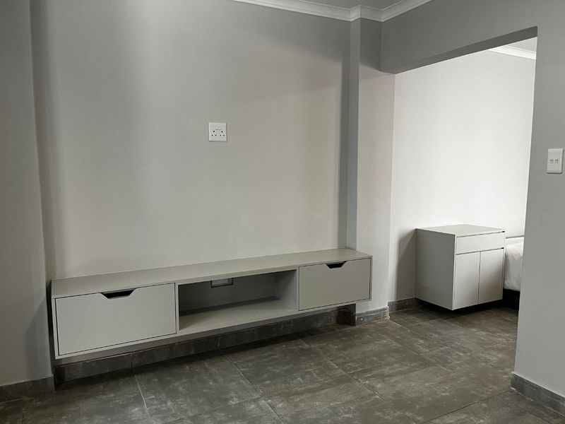 A clean, modern bedroom space featuring neutral grey walls, tiled flooring, and minimalist built-in cabinetry for storage.